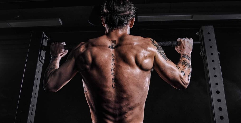 Close-up of a shirtless athlete's back muscles at the top of a pull-up, lats and traps engaged.