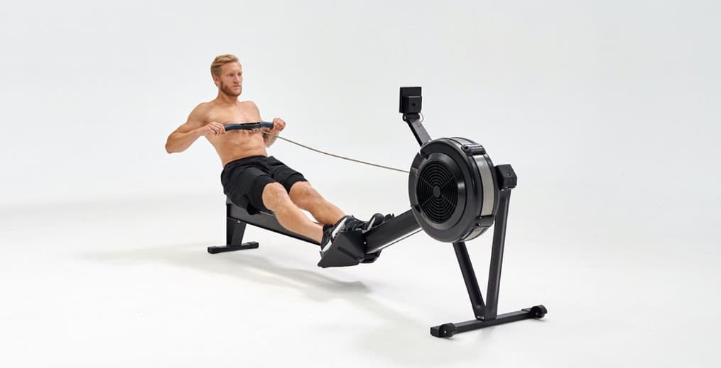A fitness athlete demonstrating the finish phase of a rowing stroke on an indoor ergometer to highlight the health benefits of rowing.