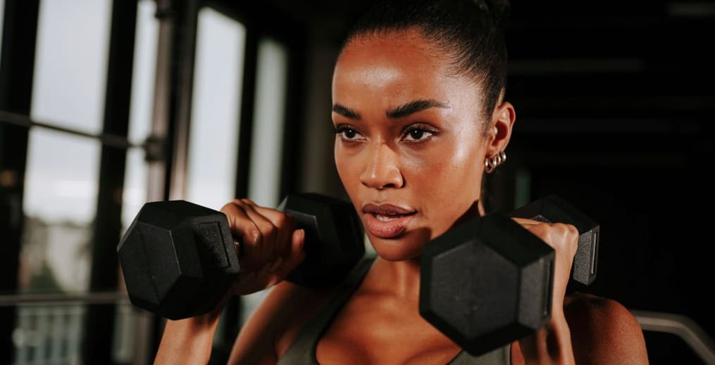 Athlete in a gym holding dumbbells, symbolizing focus and determination to achieve fitness goals.