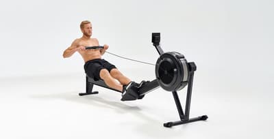 A fitness athlete demonstrating the finish phase of a rowing stroke on an indoor ergometer to highlight the health benefits of rowing.