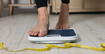 Person standing on a scale with a measuring tape on the floor, symbolizing the focus of fad diets on weight loss.