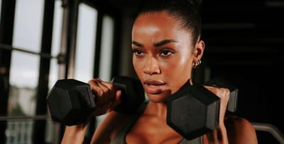 Athlete in a gym holding dumbbells, symbolizing focus and determination to achieve fitness goals.
