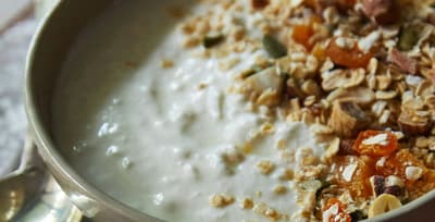 Bowl of creamy Greek yogurt topped with dried fruit and nuts on a table