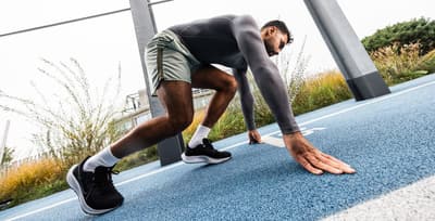 An athlete in a crouched start position on a track, demonstrating the importance of sprinting for total fitness.