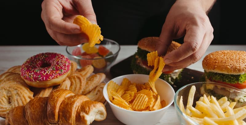 A table filled with various types of junk food, including chips, burgers, and sugary drinks.